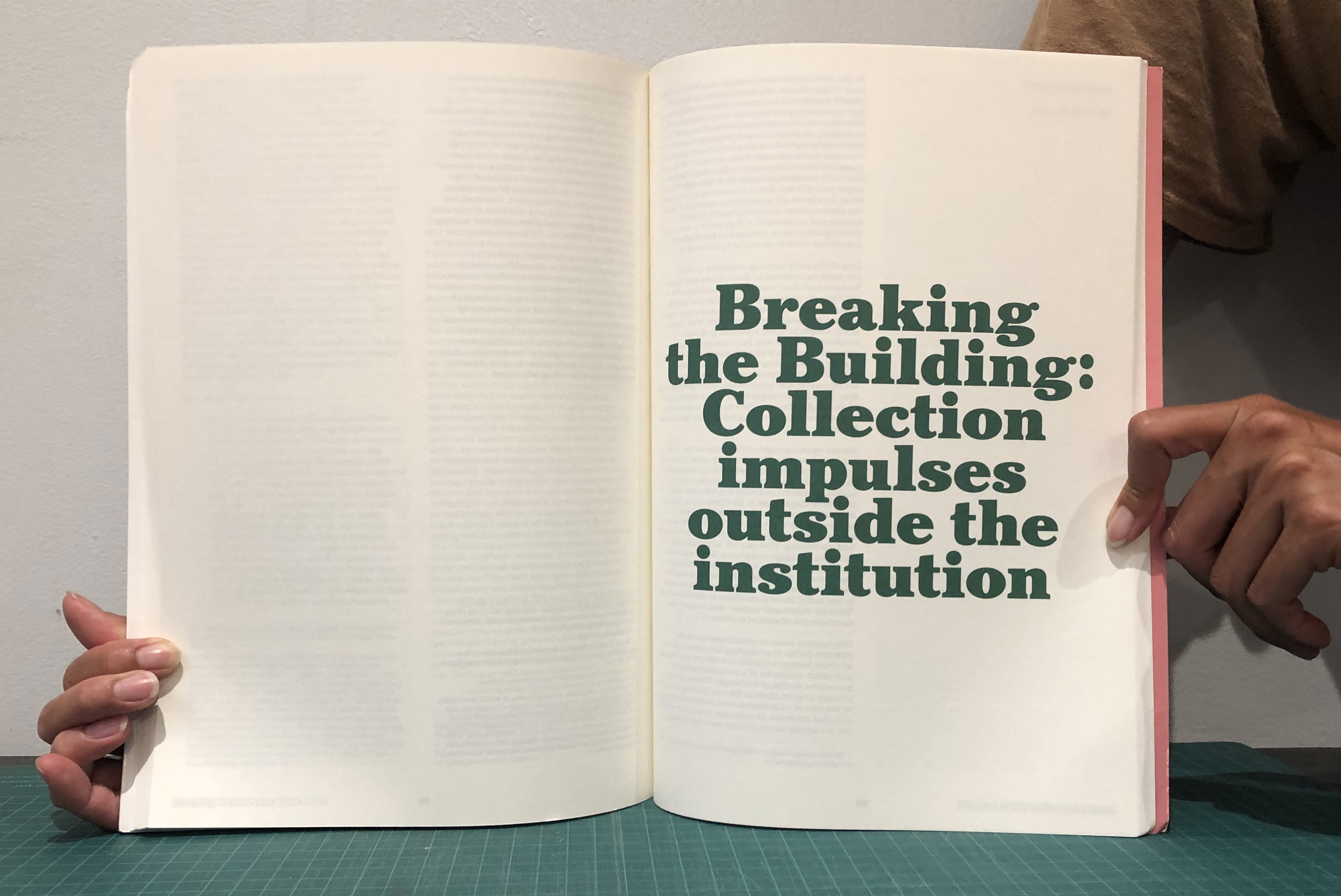 A book being held open to reveal a spread that reads “Breaking the Building: Collection impulses outside the institution” in green writing.